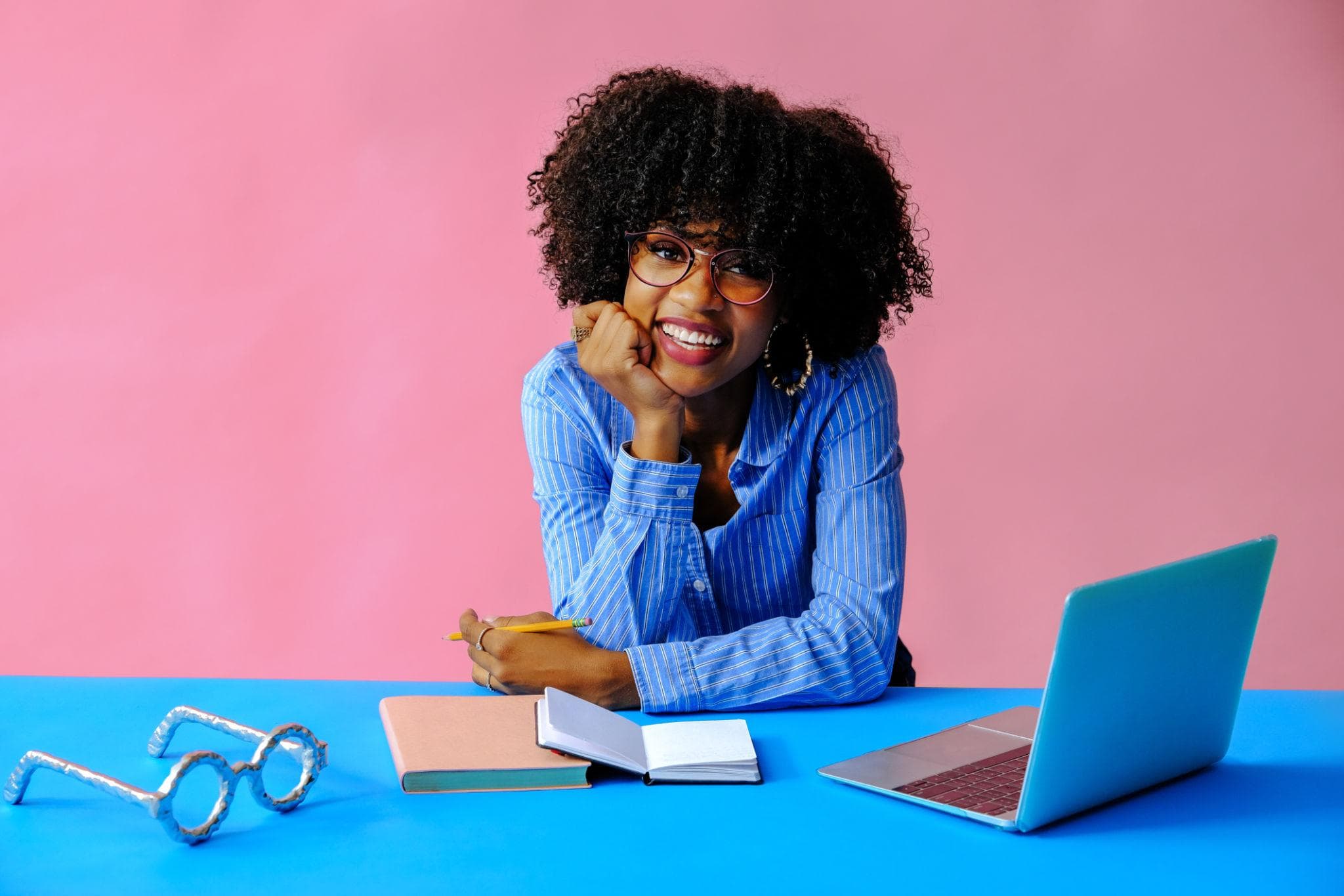 Empreendedora sorrindo à mesa com caderno, lápis e notebook