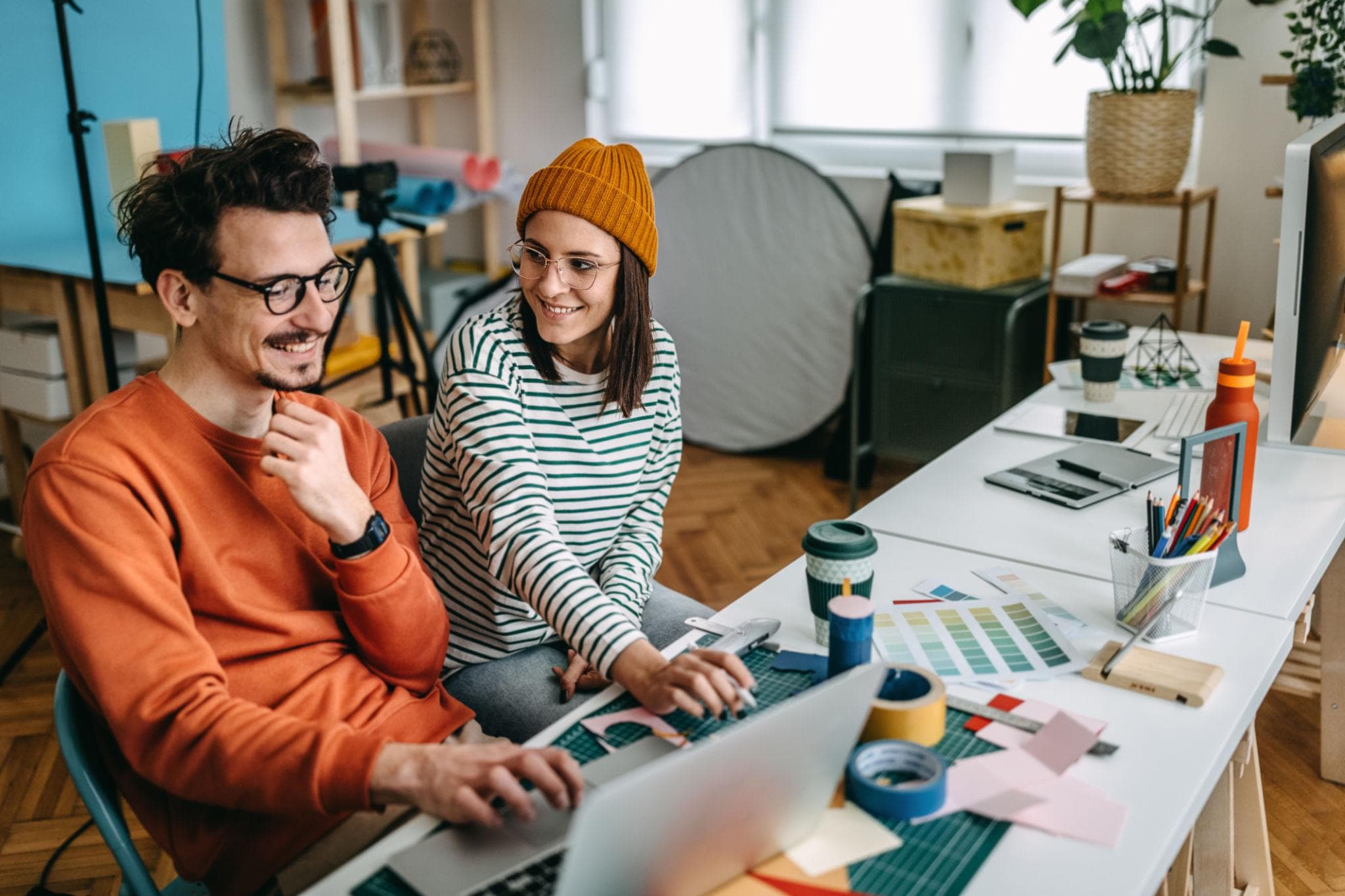 Dois sócios sorrindo em frente ao notebook no ateliê